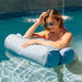 A woman in a pink bikini and sunglasses relaxes in a swimming pool using a light blue cylindrical pool float.
