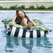 A woman reclines on a striped and tropical leaf inflatable pool float in a swimming pool.