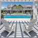 Two white Adirondack-style outdoor high density polyethylene resin chairs on a covered patio with strong window shadows, overlooking a bright blue swimming pool and a large modern gray house with a landscaped yard.