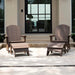 Two brown Adirondack-style outdoor high density polyethylene resin chairs with matching ottomans arranged on a patio in front of a modern building with large black-framed glass doors.