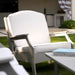 A modern outdoor high density polyethylene resin armchair with a white cushioned seat and backrest, set on green grass next to a light-colored table in a patio environment.