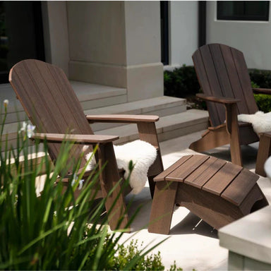 Two wooden Adirondack chairs with footstools on an outdoor patio near the staircase entrance of a modern home.