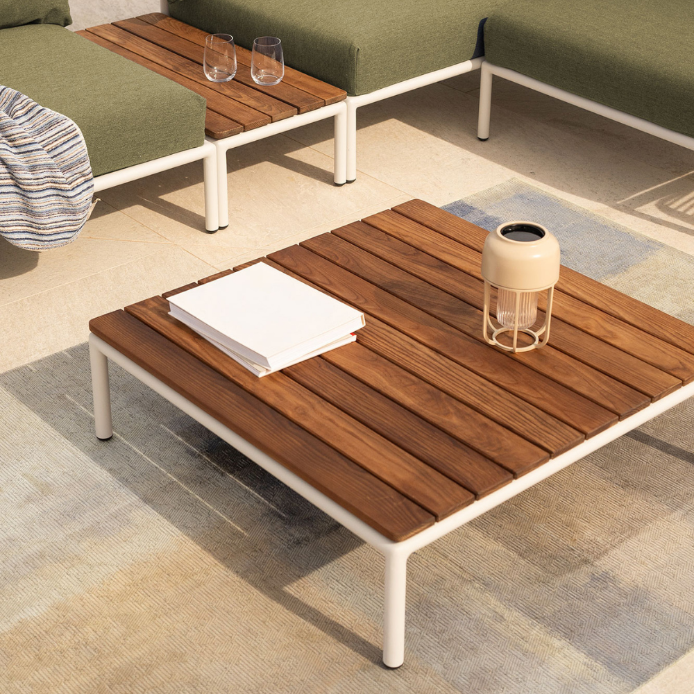 quare outdoor coffee table with a wooden top and white aluminum frame, paired with a green cushioned sectional sofa and side table accent on a tiled patio