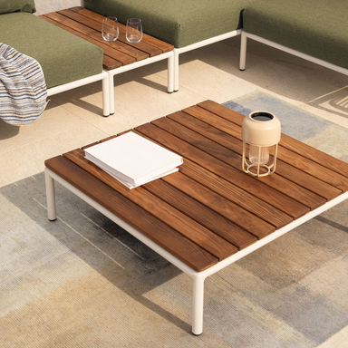 quare outdoor coffee table with a wooden top and white aluminum frame, paired with a green cushioned sectional sofa and side table accent on a tiled patio