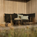 Black outdoor lounge sofa left corner with an aluminum frame, light gray pillows, and a blanket, placed on a patio against a wooden wall