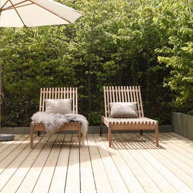 Two wooden Amaze lounge chairs on a wooden deck with an umbrella and cushions, surrounded by greenery.