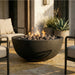 Round concrete fire pit on a patio with chairs and plants in the background