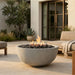 Outdoor patio with a round concrete fire pit, seating area, and plants.