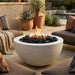 Outdoor setting with a round concrete fire pit table surrounded by patio furniture and plants.