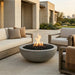 Outdoor patio with round concrete fire pit, seating area, and modern building in the background