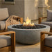 Outdoor seating area with a round concrete fire pit and chairs in a warm setting.