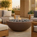 Outdoor patio setting with a round concrete fire pit table, chairs, and cityscape view.