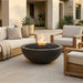 Outdoor patio setting with a round concrete fire pit, chairs, and a couch in front of a house.
