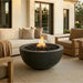 Outdoor patio with round concrete fire pit, couch, and chairs in front of a house.
