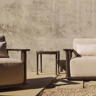 Gray cushioned outdoor lounge chair and sofa with a black side table on a concrete patio.
