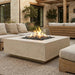 Outdoor patio with white square concrete fire pit table, seating area, and decorative elements.