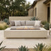 Outdoor patio with a rectangular concrete fire pit table and sofa set in a garden setting.