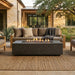 Outdoor patio with rectangular concrete fire pit table and sofa set in front of a house.
