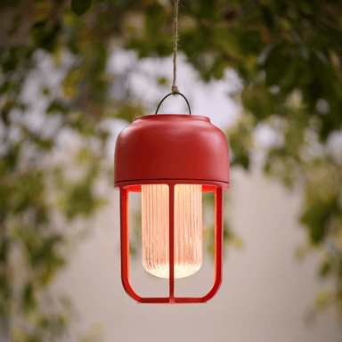 A solar-powered red portable outdoor lamp hanging on a tree branch