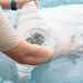 A person dipping a white in-pool chaise lounge in clear pool water.
