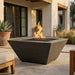 Modern outdoor black square concrete fire pit with flames in a patio setting.