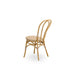Natural rattan outdoor dining side chair viewed from the angled rear with a woven wicker seat and double-loop backrest.