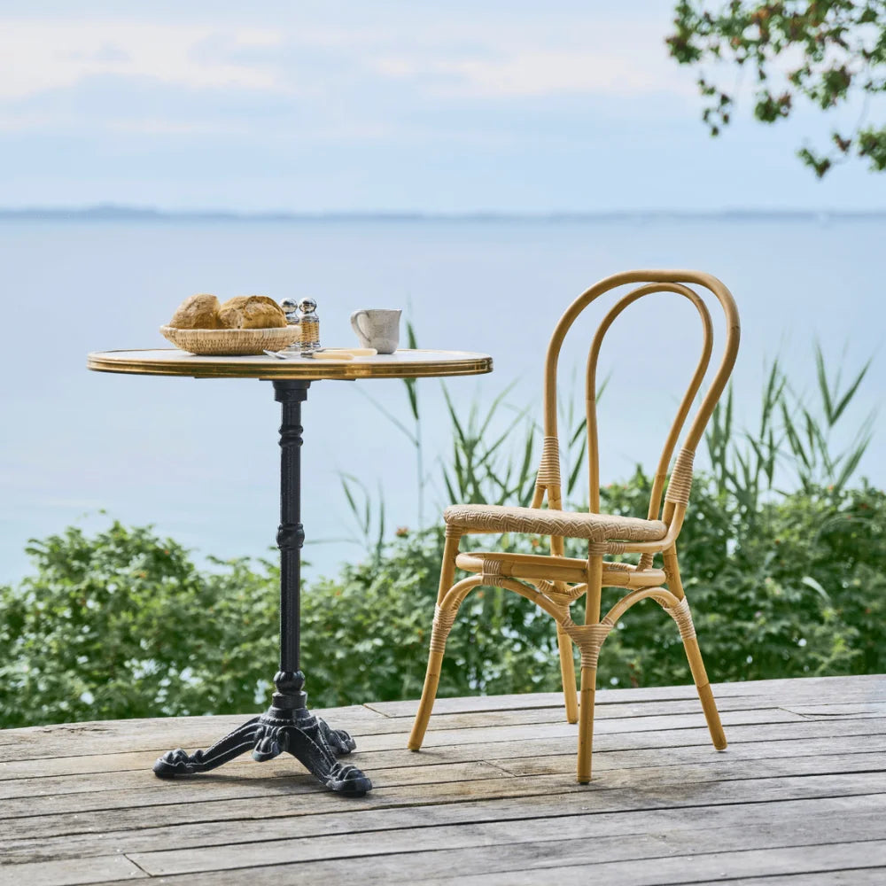 Natural rattan outdoor dining side chair with a matching round pedestal table on a seaside deck.