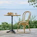 Natural rattan outdoor dining side chair with a matching round pedestal table on a seaside deck.