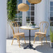 Natural rattan outdoor dining side chairs with a matching round marble-top bistro table on a patio.