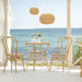 Natural rattan outdoor dining side chairs beside a matching round bistro table on a seaside patio.