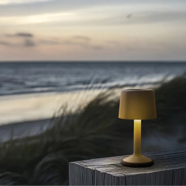 Small yellow green outdoor lamp on a wooden surface overlooking a beachfront with tall grasses