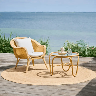Natural rattan outdoor lounge chair with white cushions beside a matching round coffee table by the sea.