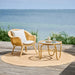 Natural rattan outdoor lounge chair with white cushions beside a matching round coffee table by the sea.