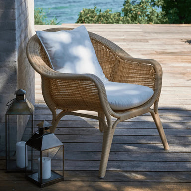 Natural rattan outdoor lounge chair with white cushions on a wooden deck overlooking the ocean.