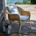 Natural rattan outdoor lounge chair with white cushions on a wooden deck overlooking the ocean.