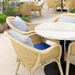 Natural rattan outdoor lounge chair with blue and white cushions beside a round marble-top dining table.