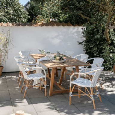 White rattan outdoor dining armchair with a woven seat and back beside a matching wooden dining table.