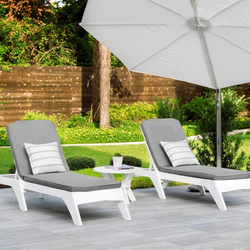 Two white outdoor chaise lounge chairs with gray cushions and striped pillows, set on a patio under a large white patio umbrella in a garden backyard.