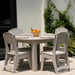 A round outdoor dining table set with four matching light gray chairs, shown on a patio with tableware and a bowl of oranges in the center.