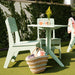 A mint green outdoor patio dining set consisting of a square table and two matching chairs, styled on artificial grass with a straw basket, drinks, and a yellow flower arrangement.
