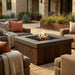 Outdoor patio with square outdoor concrete fire pit table with an element of teak slats, chairs, and decorative plants.