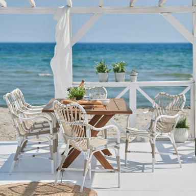 White rattan outdoor dining armchair with a woven seat and back beside a matching wooden dining table.