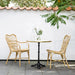 Natural rattan outdoor dining armchair beside a matching round marble-top bistro table on a patio.