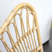 Close-up of a natural rattan outdoor dining armchair featuring an open slatted backrest.