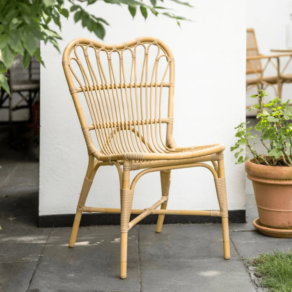Natural rattan outdoor dining armchair featuring an open slatted back in a garden patio setting.