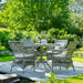 Gray rattan outdoor dining armchairs with white cushions around a matching round dining table in a garden.