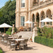 Gray rattan outdoor dining armchairs with white cushions around matching round dining tables on a garden patio.