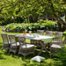 Gray rattan outdoor dining side chair with white cushions beside a matching rectangular dining table in a garden.