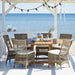 Gray rattan outdoor dining side chair with white cushions beside a matching wooden dining table by the ocean.
