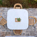 Top view of white rounded square outdoor dining table and four wooden chairs on a stone floor